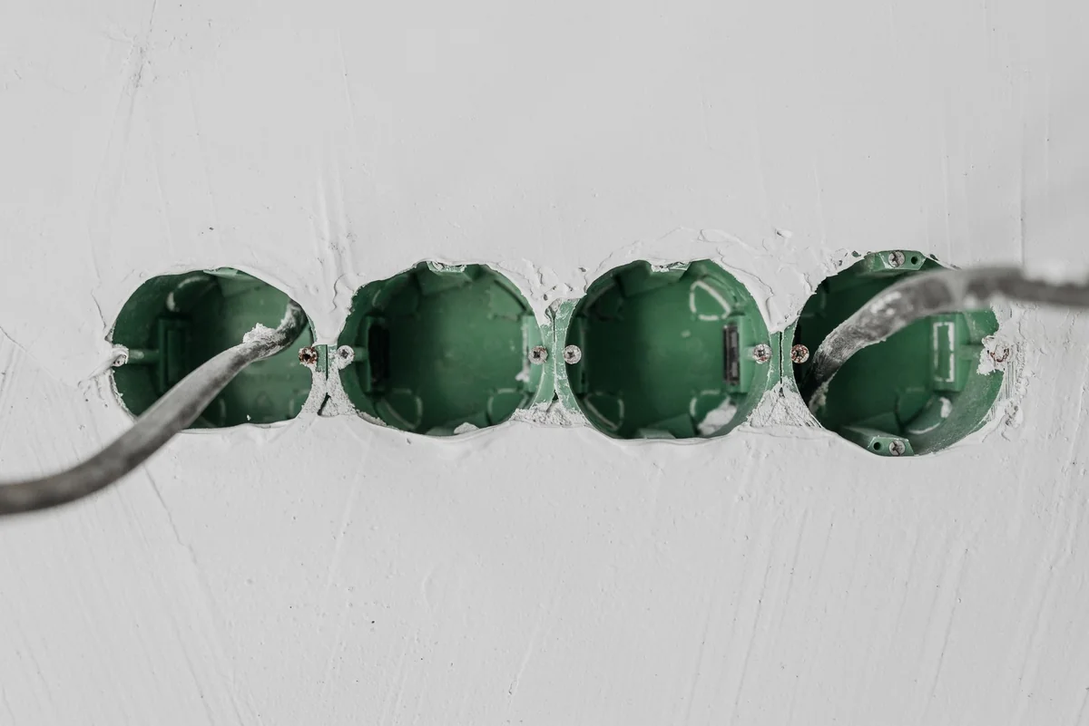 Four green electrical boxes set into an unfinished white wall, two with cables pulled through