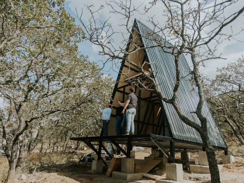 Wooden A-frame cabin under construction in a wooded area