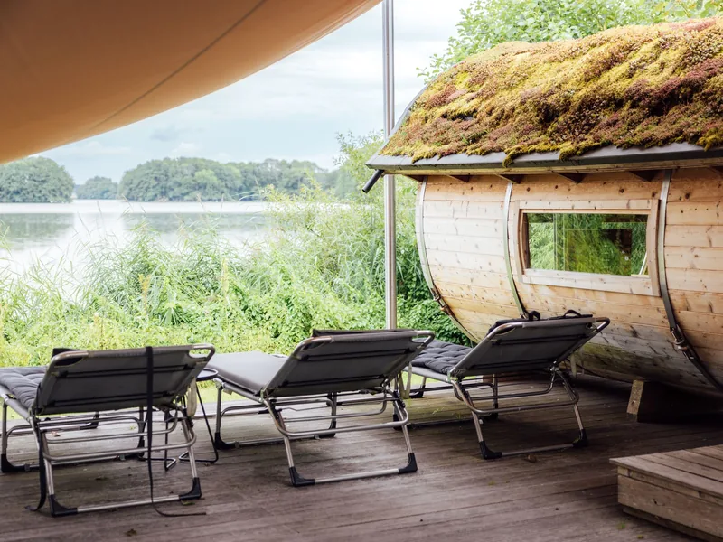 Barrel sauna with a moss roof beside a lake